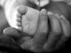 A parent's hand holds the tiny foot of a small baby