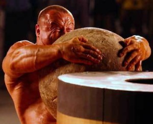 An exceptionally strong man lifting a stone ball onto a high wooden stand